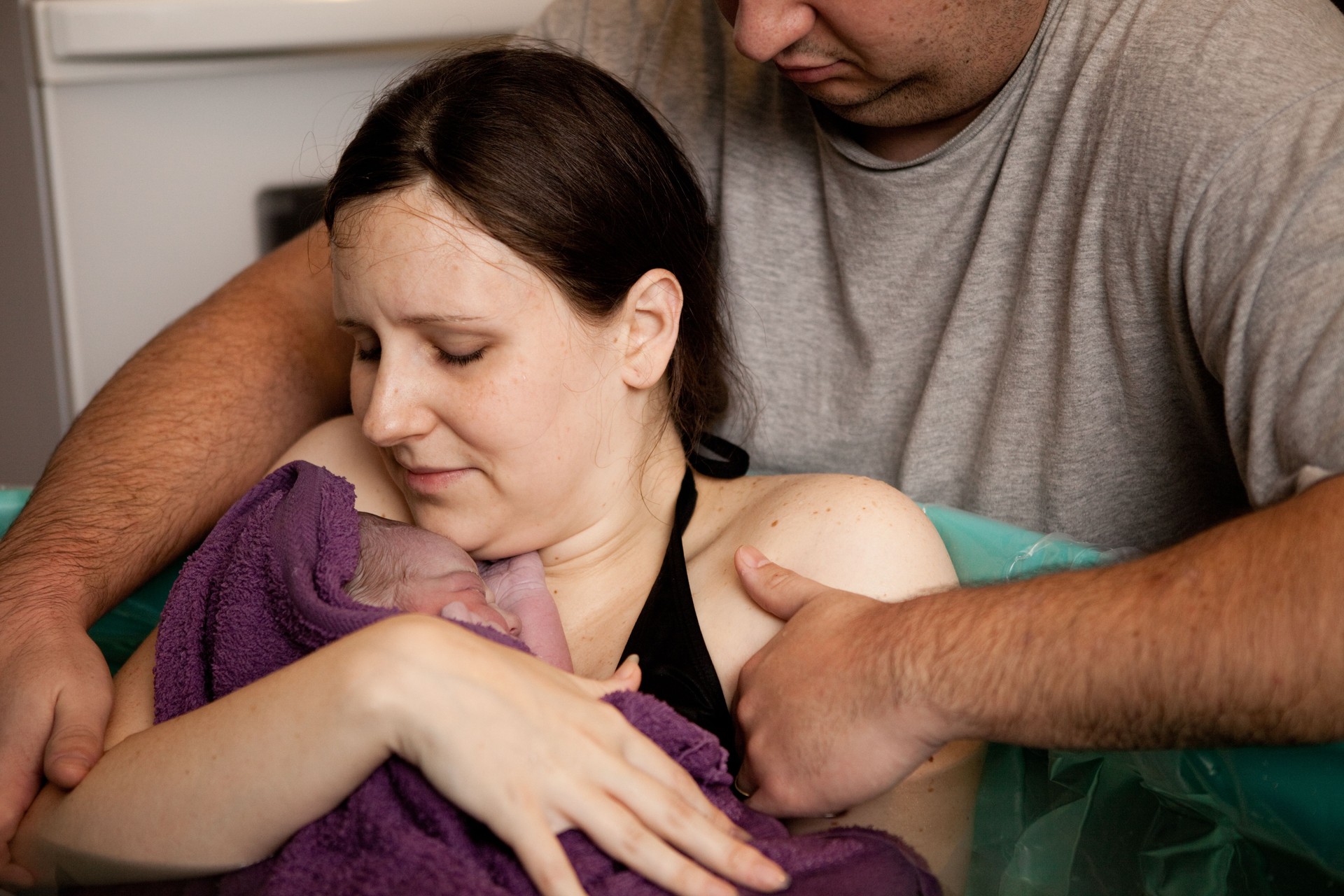 Husband Comforting Wife Holding Newborn after Home Water Birth