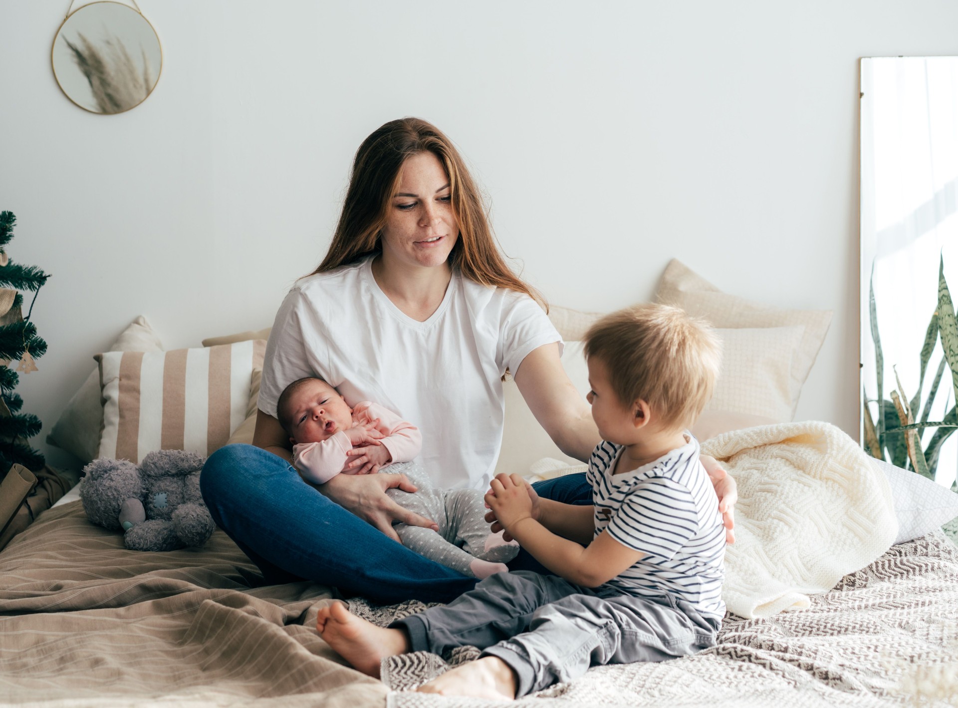 A young mother with two small children spends time in the bedroom at home.